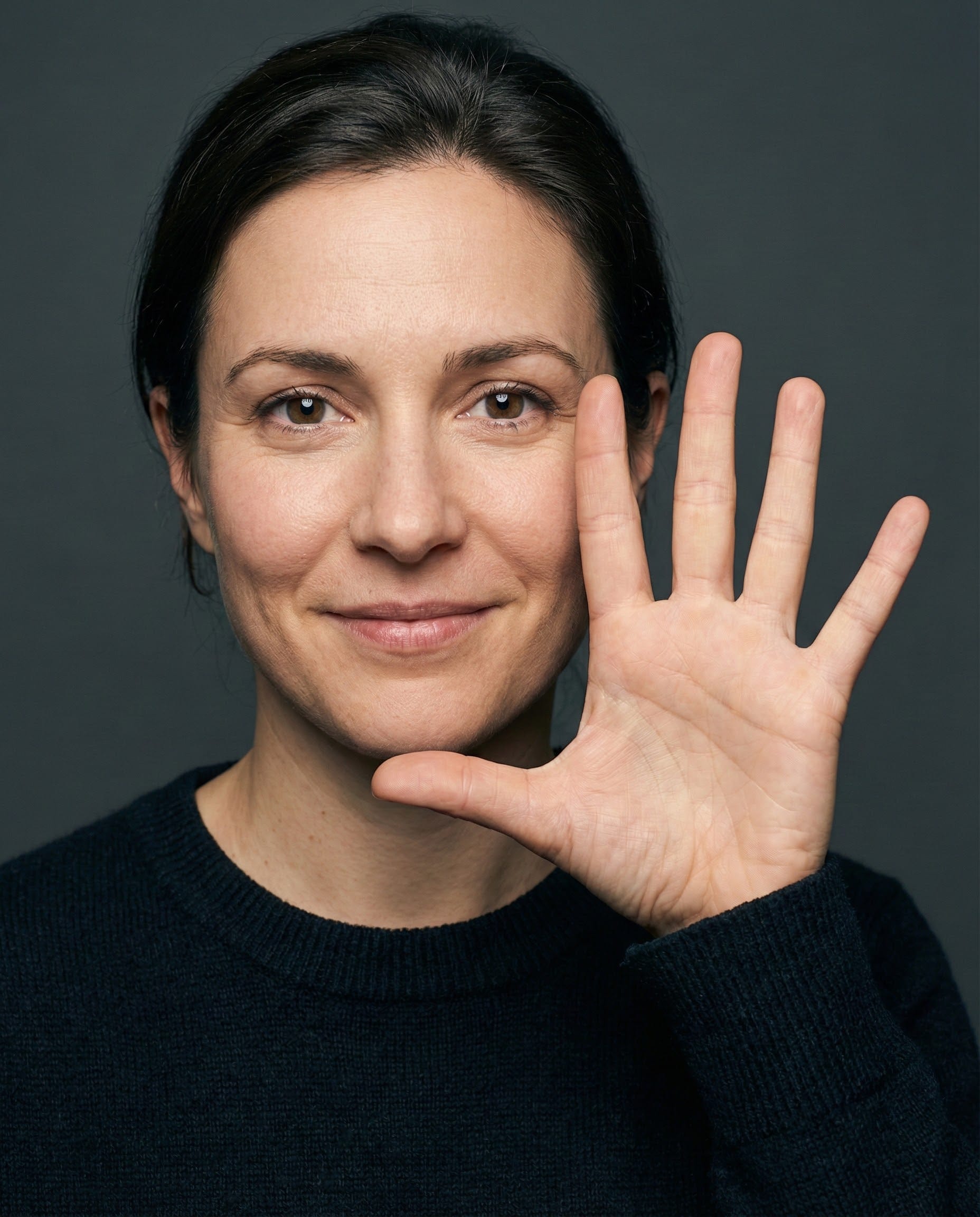 Photorealistic portrait of a woman holding her hand up to her face, open palm facing the camera, all five fingers clearly visible, studio lighting, 8K resolution